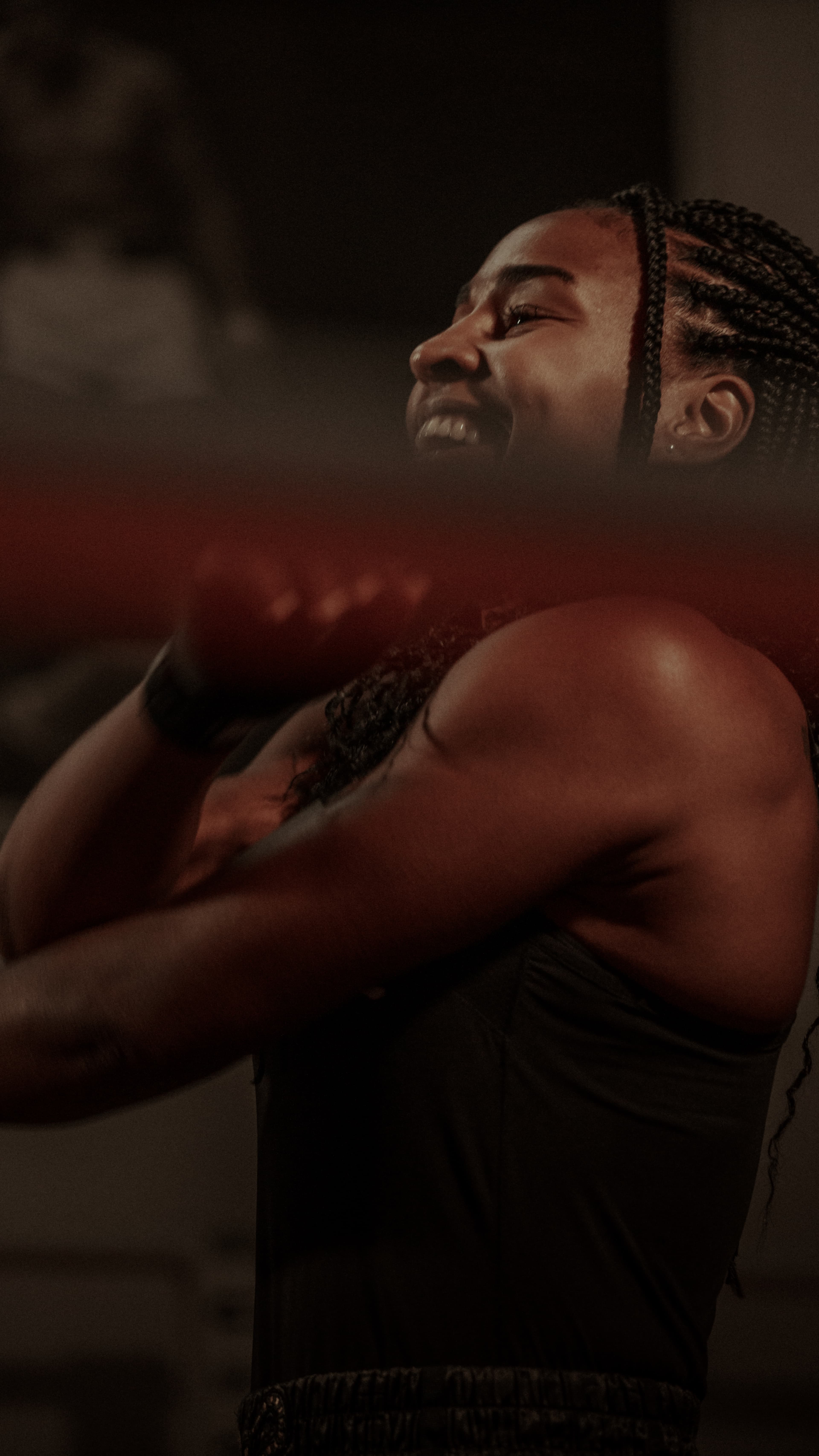 Boxeuse souriante en mouvement derrière une corde de ring, plan serré sur l’épaule et le buste