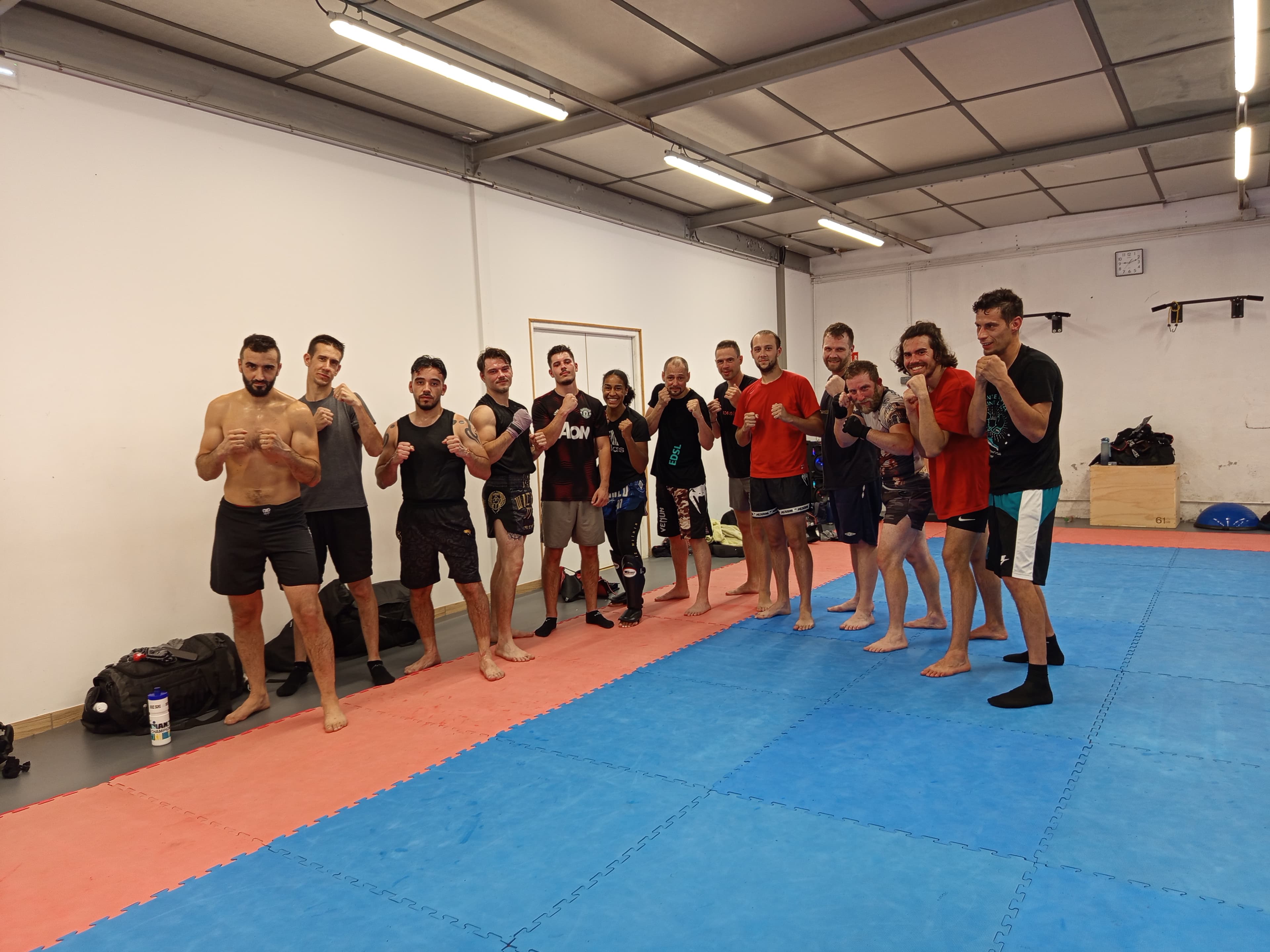 Groupe de pratiquants de kick-boxing posant ensemble en garde sur un tatami dans une salle de sport