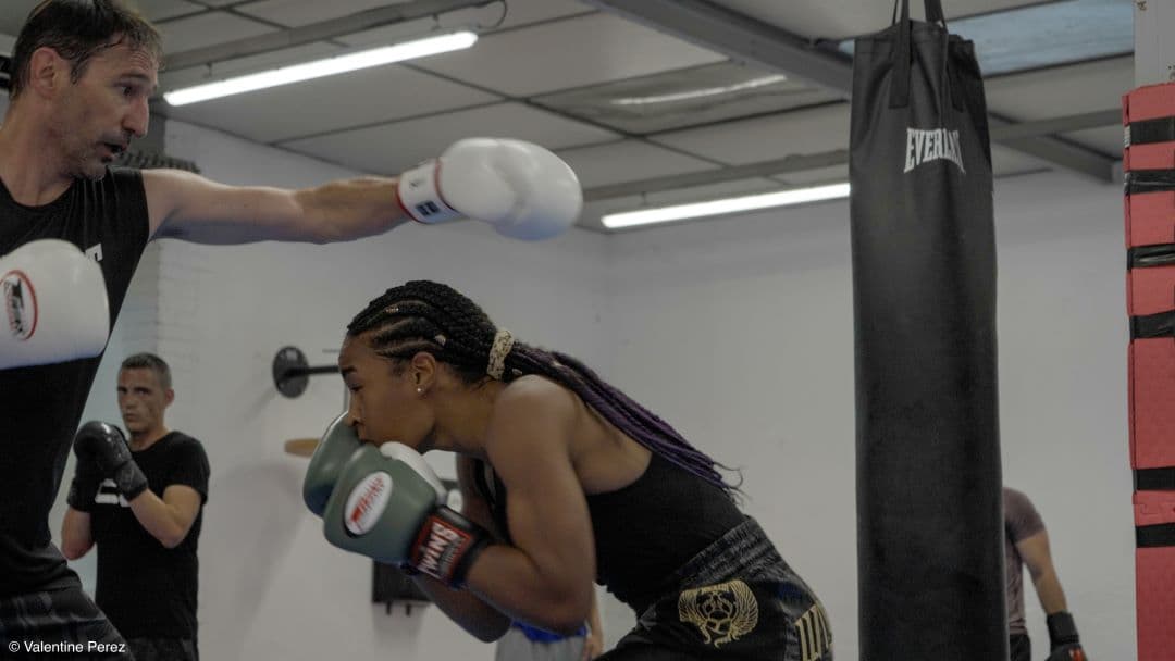 Scène dynamique d'entraînement de kick-boxing : une femme esquive un coup lors d’un sparring