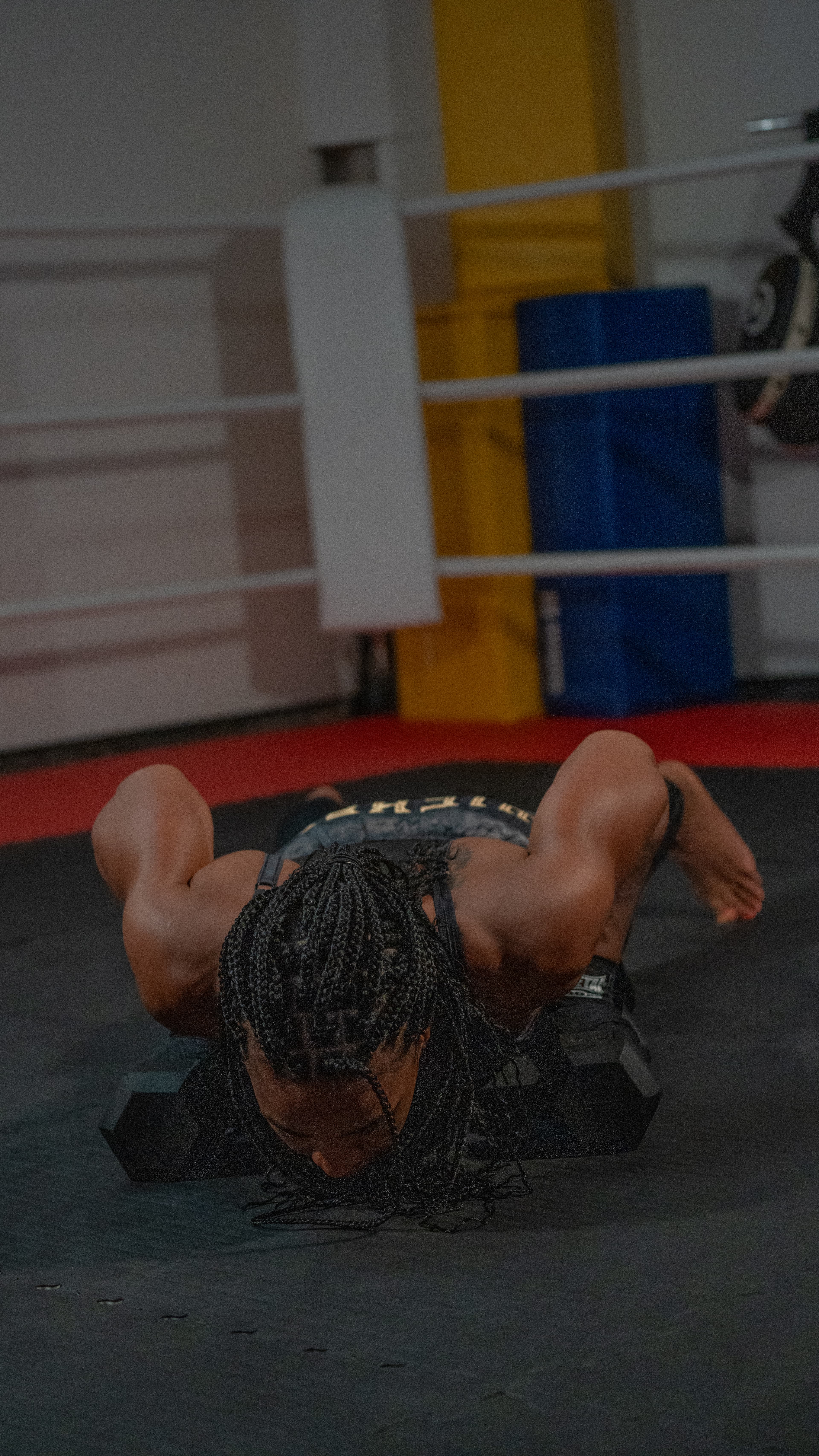 Personne en short de boxe noir et doré, faisant un exercice de corde ondulatoire, gantée de bandes de boxe, dans un ring de boxe.